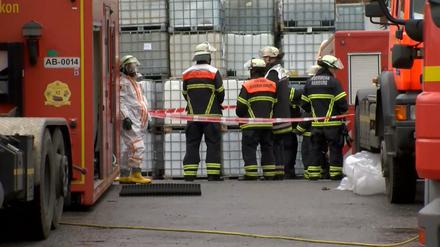 Einsatzkräfte der Feuerwehr stehen in Schutzanzügen vor einer Lagerhalle im Hamburger Stadtteil Steinwerder.