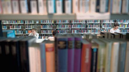 Doch erst einmal nicht gratis. Besucher der Amerika Gedenkbibliothek in Berlin sitzen am zwischen Bücherregalen. 