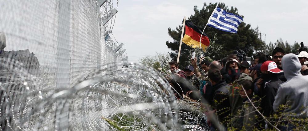 Flüchtlinge mit einer griechischen und einer deutschen Nationalfahne am Grenzzaun zu Mazedonien am Montag. 