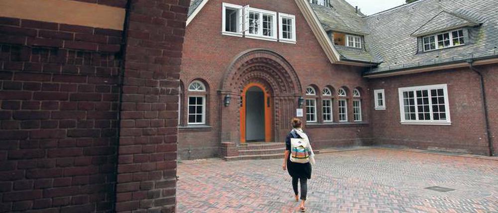 Eine junge Frau geht über den Innenhof eines historischen Gebäudes auf eine Tür zu.