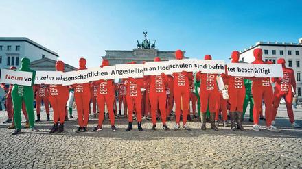 Menschen in roten Ganzkörperanzügen mit dem Schriftzug "befristet" stehen vor dem Brandenburger Tor.