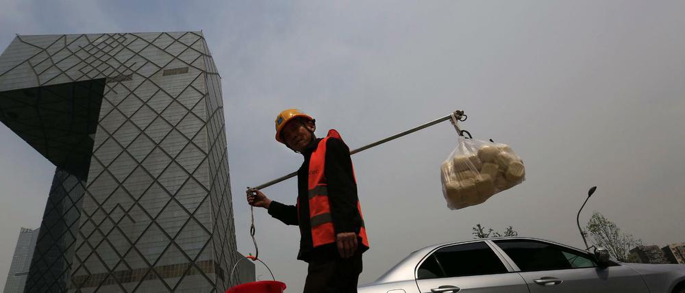 Ein chinesischer Bauarbeiter geht an einem der markantesten Bauwerken in Peking vorbei, dem Gebäude des chinesischen Staatsfernsehens CCTV.