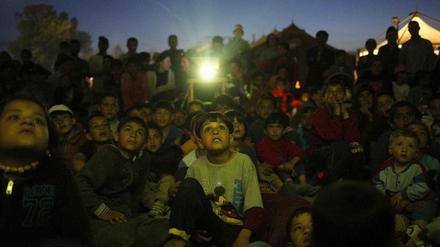 Kinder in Idomeni schauen einen Film auf einer Leinwand.