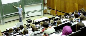 Ein junger Dozent steht in einem Hörsaal an der Tafel und erklärt Formeln.