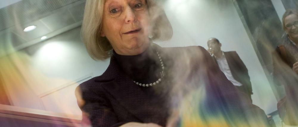 Eine Frau hält Ihre Hand in einen künstlich erzeugten Regenbogen und verzieht dabei das Gesicht.