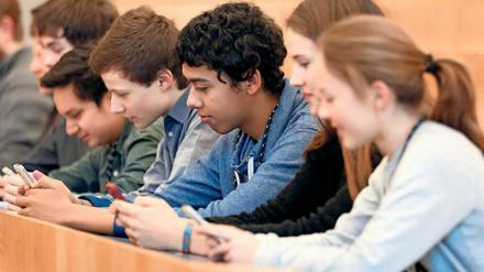 Jugendliche sitzen in einer Reihe an einem Arbeitstisch und hantieren mit ihren Smartphones.