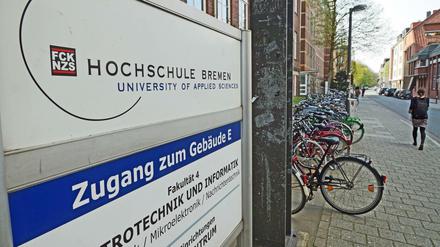 Ein Hinweisschild weist ein Hochschulgebäude als Fakultät für Elektrotechnik und Informatik aus, auf dem Gehweg davor ist eine Passantin zu sehen.