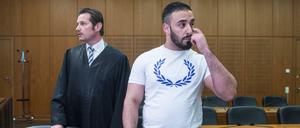 Mit einem weißen T-Shirt bekleidet steht der Angeklagte Aria L. in einen Hochsicherheitssaal des Oberlandesgerichts in Frankfurt am Main neben seinem Anwalt Andreas Bensch.