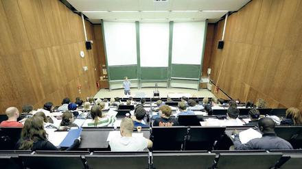 Ein junger Dozent steht vor Studierenden, die in einem Hörsaal sitzen.