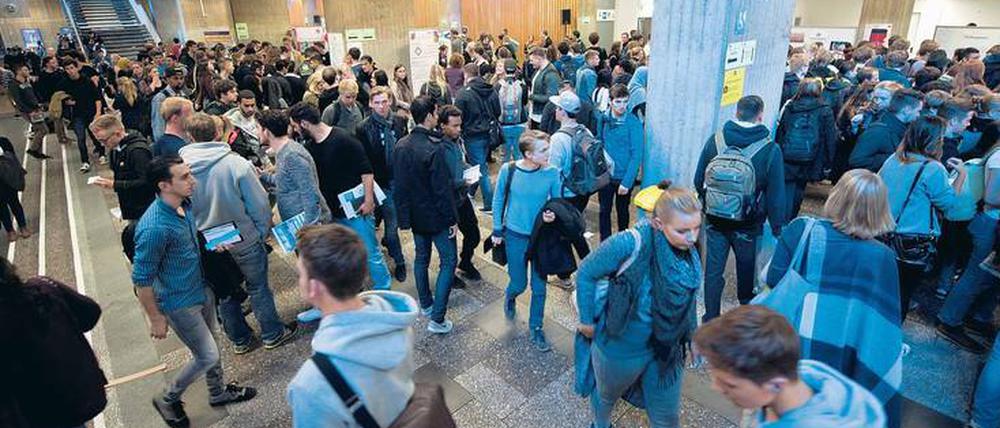 Viele junge Frauen und Männer gehen durch das Foyer einer Universität.