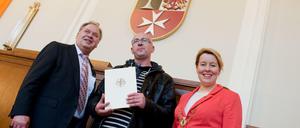 Der aus Polen stammende Kamil (M) steht am 25.04.2016 in Berlin im Rathaus Neukölln nach der Einbürgerungszeremonie zwischen dem Parlamentsvorsteher Jürgen Koglin (SPD) und der Bezirksbürgermeisterin von Neukölln, Franziska Giffey (SPD). 