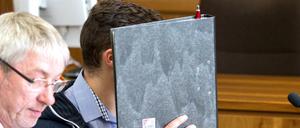 Der 25-jährige angeklagte Feuerwehrmann sitzt am Dienstag in Hagen im Landgericht mit einem Aktenordner vor dem Gesicht im Gerichtssaal neben seinem Anwalt Andreas Trode.