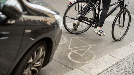 Eine Radfahrerin umfährt ein auf dem Radweg stehendes Auto. 