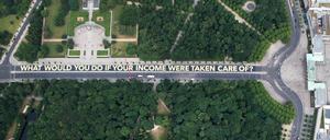 "WHAT WOULD YOU DO IF YOUR INCOME WERE TAKEN CARE OF?" steht auf dem riesigen Plakat auf der Straße des 17. Juni zwischen der Siegessäule und dem Brandenburger Tor in Berlin. 