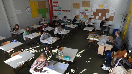 Ein Lehrer sitzt an seinem Pult vor der Klasse.