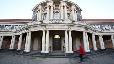 Eine Frau in roter Jacke fährt auf einem Fahrrad vor dem Hauptgebäude der Universität Hamburg entlang.