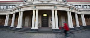Eine Frau in roter Jacke fährt auf einem Fahrrad vor dem Hauptgebäude der Universität Hamburg entlang.