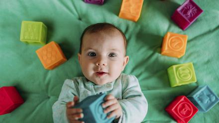 Portrait of baby girl lying on green mat playing with rubber toys model released Symbolfoto PUBLICATIONxINxGERxSUIxAUTxHUNxONLY GEMF03420