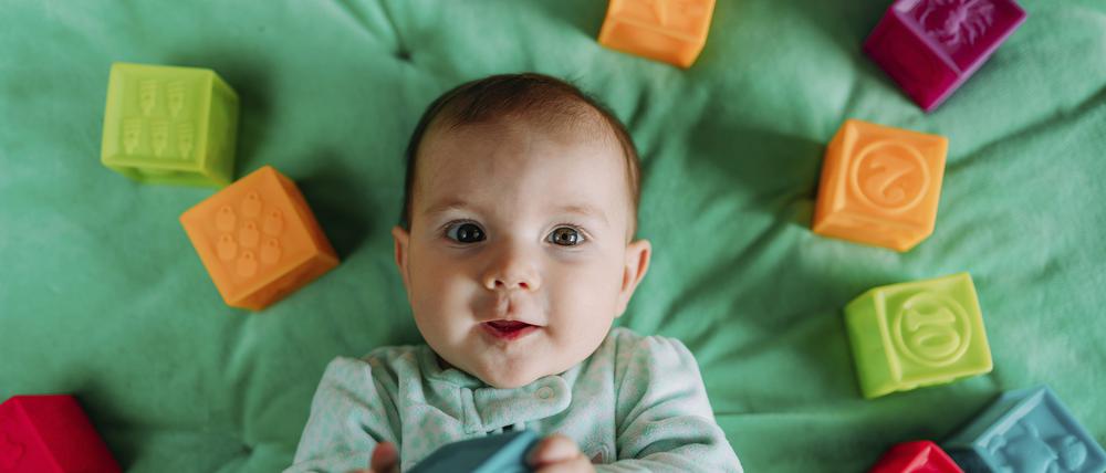 Portrait of baby girl lying on green mat playing with rubber toys model released Symbolfoto PUBLICATIONxINxGERxSUIxAUTxHUNxONLY GEMF03420