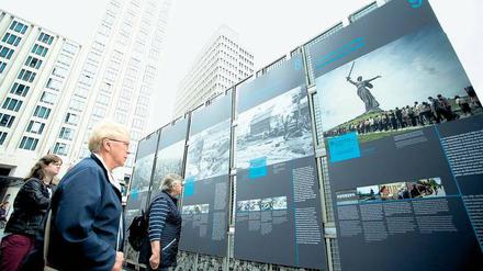 Menschen stehen vor Plakatwänden einer Freiluftausstellung und lesen die Texte.