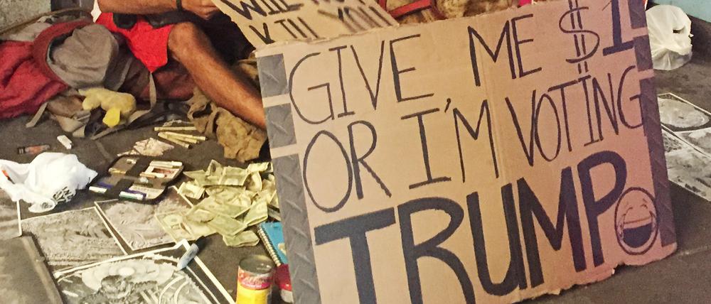 Ein Bettler in New York mit einem Schild mit der Aufschrift "Give me $1 or I'm voting Trump!" (Gib mir 1 Dollar oder ich stimme für Trump) aufgestellt.