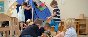 Sieben Kinder spielen in einer Kita mit einer Holzeisenbahn und in einem Zelt.