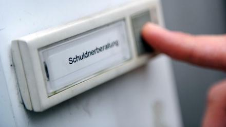 Klingelschild einer Schuldnerberatung mit Finger, der auf Klingelknopf drückt.