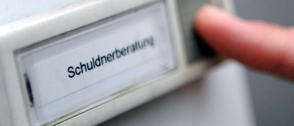 Klingelschild einer Schuldnerberatung mit Finger, der auf Klingelknopf drückt.