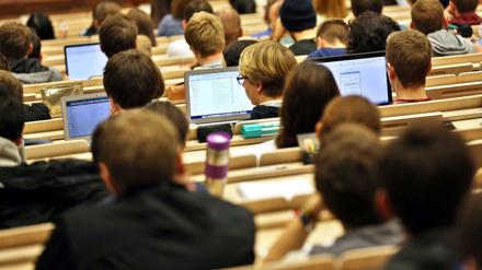 Studierende sitzen im Hörsaal vor aufgeklappten Laptops.
