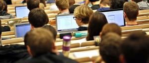 Studierende sitzen im Hörsaal vor aufgeklappten Laptops.