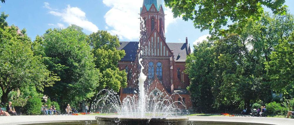 Blick von Westen auf die Grünanlage des Ludwigkirchplatzes in Berlin-Wilmersdorf mit dem Brunnen vorn und der katholischen Kirche St. Ludwig im Hintergrund.