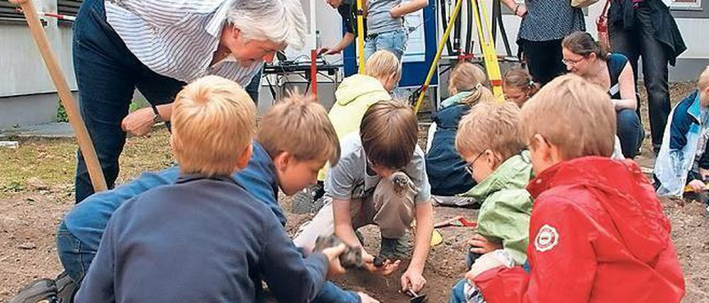 Eine Frau beugt sich über eine Gruppe von Kindern, die im Erdreich nach etwas suchen.