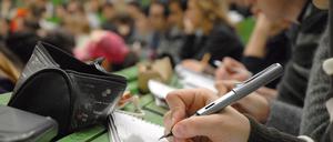 Studierende sitzen im Hörsaal und schreiben in ihre Hefte.