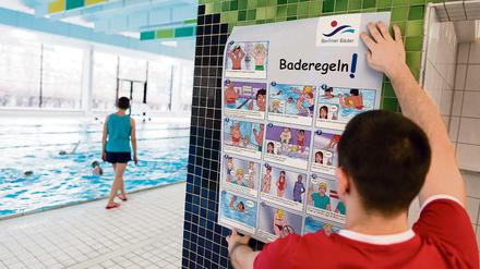 Ein Bademeister hängt am 08.02.2016 in der Schwimmhalle Fischerinsel in Berlin Plakate mit einer Darstellung der Baderegeln der Berliner Bäderbetriebe im Comic-Stil auf.
