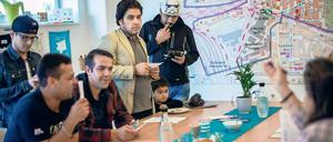 Flüchtlinge und Helfer sitzen und stehen zusammen an einem Tisch.