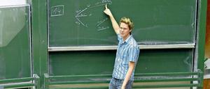 Ein junger Mann steht in einem Hörsaal vor einer Tafel und erklärt Formeln.