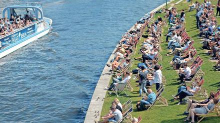 Menschen sitzen auf Liegestühlen an einem Flussufer.