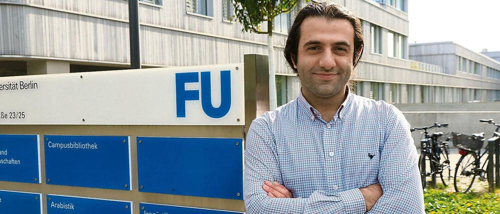 Ein Mann steht vor einem Hinweisschild der Freien Universität, im Hintergrund ist ein Universitätsgebäude zu sehen.