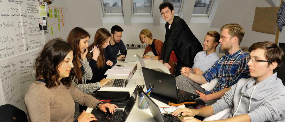 Junge Menschen sitzen in einem Raum und arbeiten an Laptops.