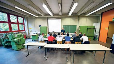 Jugendliche sitzen an Schultischen in einem Raum, in dem auch Werkzeugmaschinen stehen.