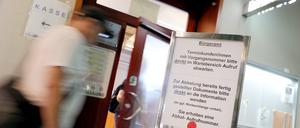 Menschen gehen im Rathaus Spandau im Bürgeramt an einem Hinweisschild für die Terminvergabe vorbei.