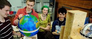 Drei junge Männer bauen einen Versuch auf, zwei junge Frauen sehen ihnen dabei zu.