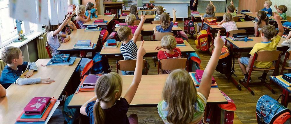 Blick ins Klassenzimmer einer Grundschule, Schüler melden sich,  vorn an der Tafel steht die Lehrerin.