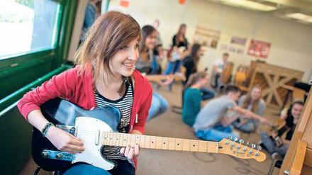 Eine junge Frau sitzt in einem Klassenzimmer und spielt Gitarre.