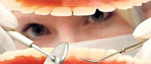 Eine Zahnmedizinerin hantiert mit Spiegel und Haken in einer offenen Mundhöhle.