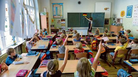 Erstklässler sitzen in einem Klassenraum und melden sich eifrig.
