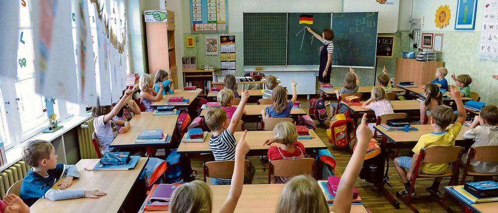 Erstklässler sitzen in einem Klassenraum und melden sich eifrig.