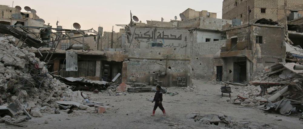 Ein Junge steht in Aleppo zwischen zerbombten Wohnhäusern.