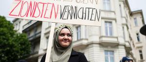 Eine Frau hält ein Plakat mit der Aufschrift "Blumen verzaubern, Zionisten vernichten" hoch.