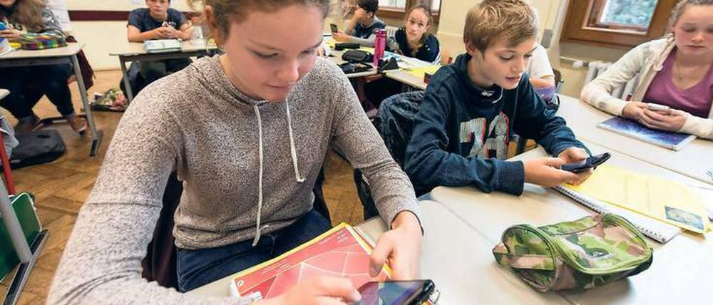 Schülerinnen und Schüler sitzen in einer Klasse und arbeiten mit ihren Smartphones.
